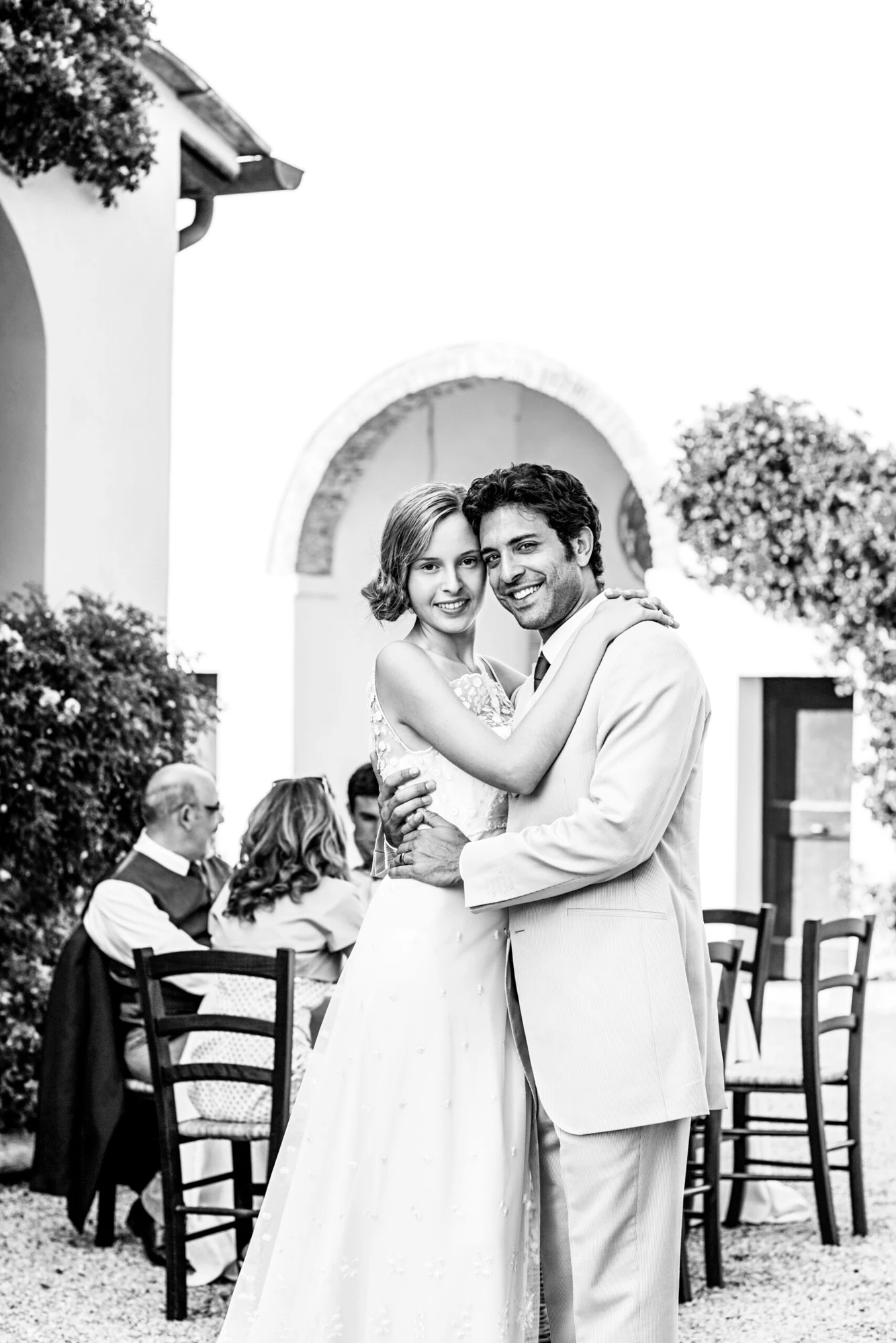 Newlyweds embracing in a flower-filled courtyard — original black-and-white edit